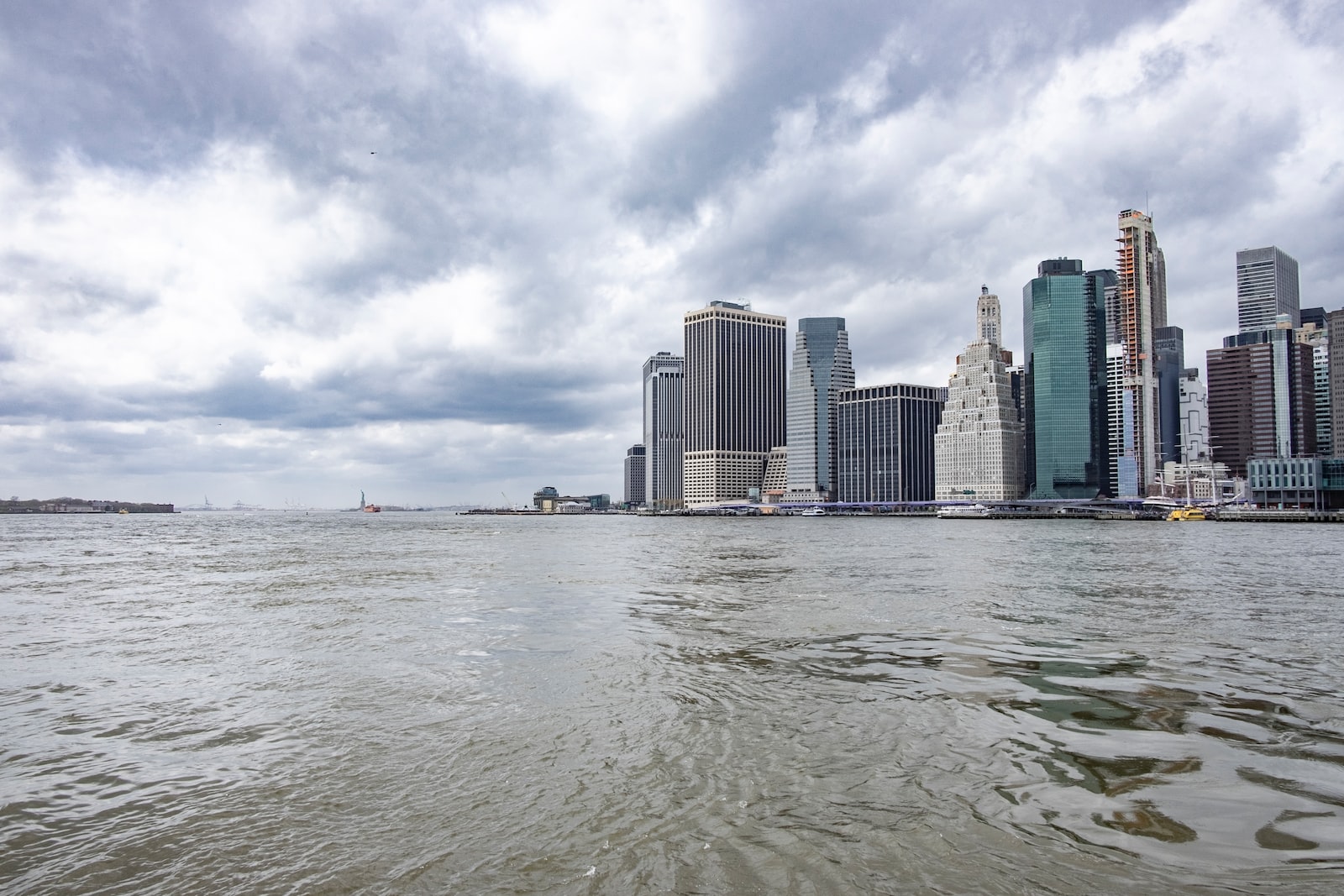 body of water near city buildings under white clouds and blue sky during daytime